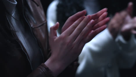 beautiful slow motion close-up shot of the hands of 3 male and female jurors applauding an audition inside a theater with low key lighting.