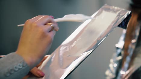 hair salon stylist applies color to foil before putting on hair of customer