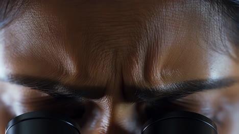 close-up of a person looking through a microscope with intense focus