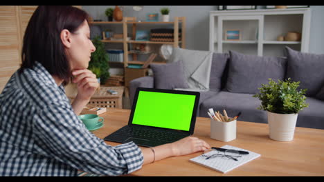 woman working from home on a laptop with a green screen