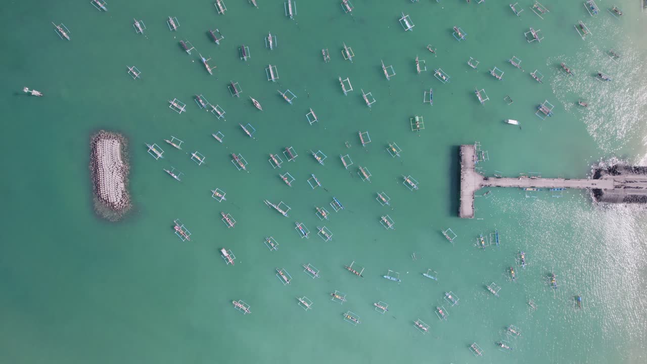 Aerial view of many Indonesian traditional juking boats bobing on turquoise transparent waves near a pier on a tropical island of Bali