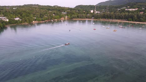 Drone-aerial-over-boat-driving-on-tropical-blue-ocean-in-Thailand-in-a-green-mountainside