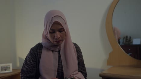mujer musulmana asiática indonesia en hijab alcanza el bolsillo para el teléfono y comienza a enviar mensajes de texto mientras está sentada