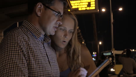 young couple with tablet pc on bus stop at night