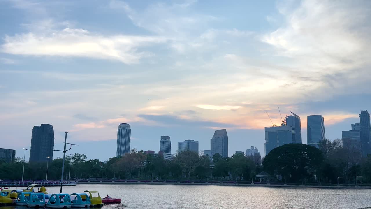 방의 벤자키티 공원 위의 조용한 일몰 풍경, 활기찬 색으로 스카이 라인과 조용한 연못을 포착합니다.