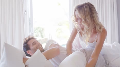 pareja teniendo una pelea de almohadas en la cama