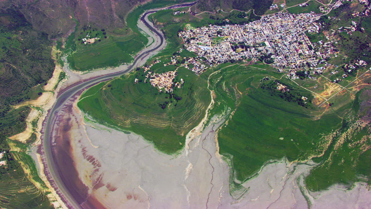 vista aérea sobre el río que fluye en las montañas y el pueblo rodeado de granjas verdes, miles de casas repartidas en el valle