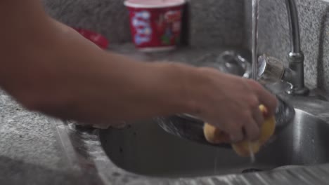 an adult washing pan with sponge and soap in the kitchen sink - medium shot