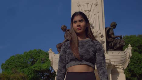 fitness girl in workout clothes walks fiercely at a park with an amazing statue in the background