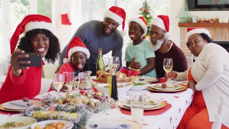 Afroamerikanische-Familie-In-Weihnachtsmützen-Macht-Ein-Selfie-Mit-Dem-Smartphone,-Während-Sie-Am-Esstisch-Sitzt-Ha