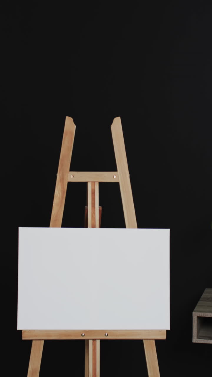Vertical video of white canvas sign on wooden easel with copy space on black background