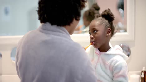 happy african american mother and daughter brushing teeth and kissing in bathroom, slow motion