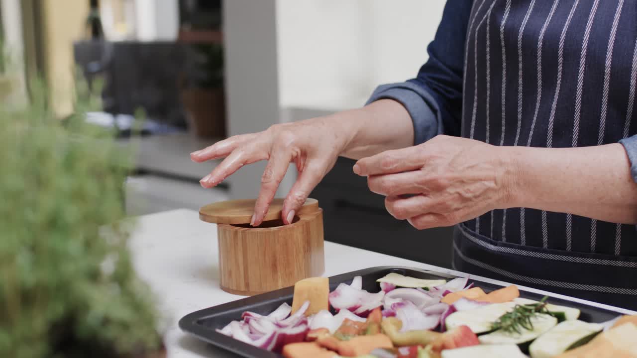 sección media de una mujer caucásica mayor sazonando verduras en la cocina, cámara lenta
