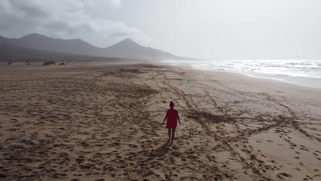 a woman walks alone on a sunny fuerteventura beach with hazy skies