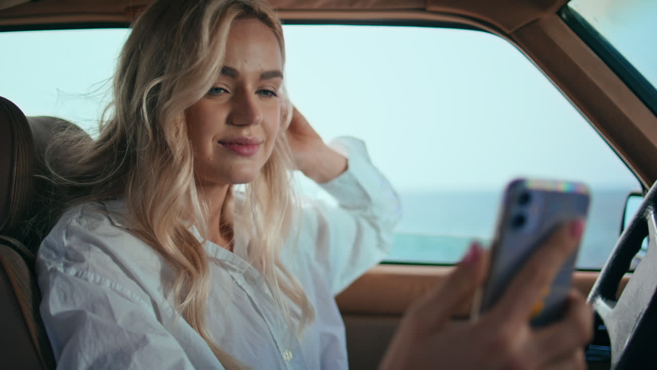 Ragazza che registra un video blog seduta in auto, primo piano. Donna che guarda la fotocamera dello smartphone.