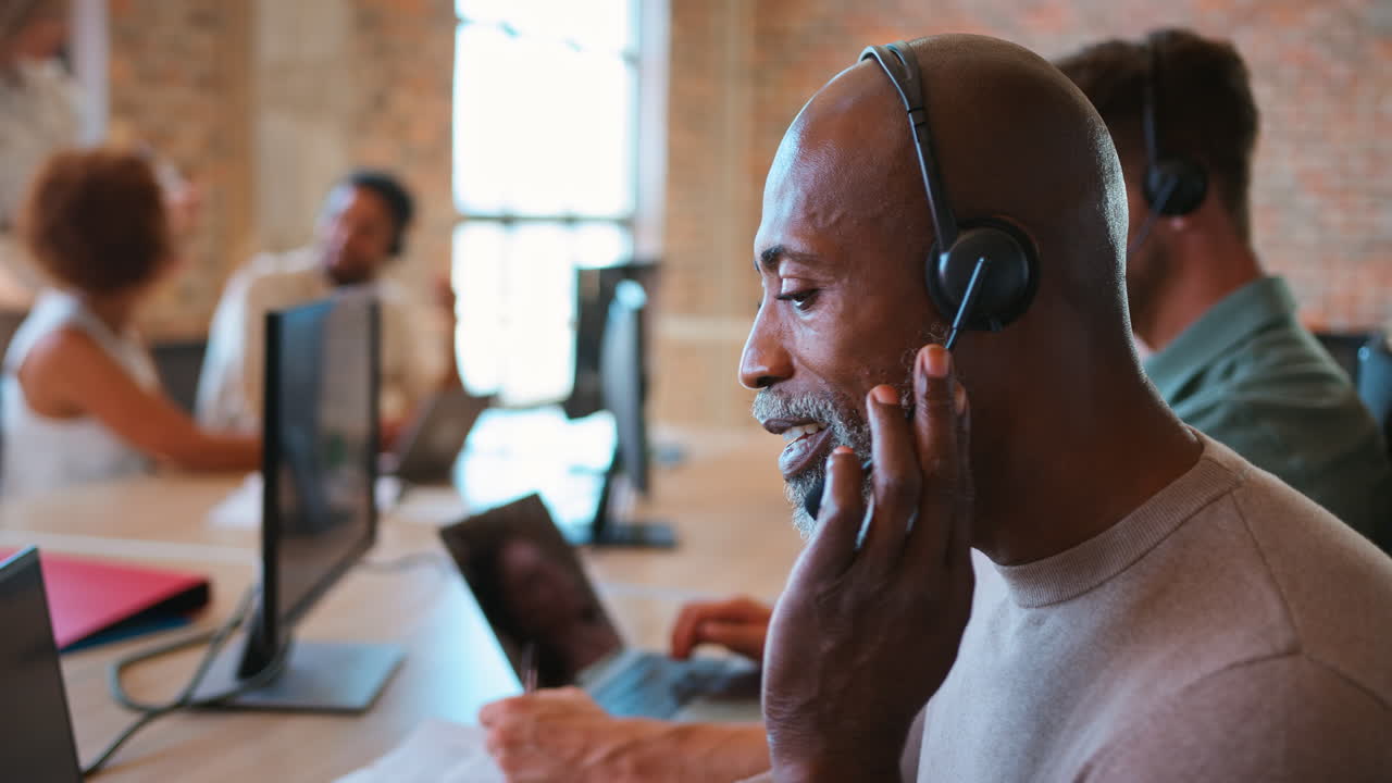 Mature Businessman In Multi-Cultural Business Team Wearing Headset In Customer Support Centre