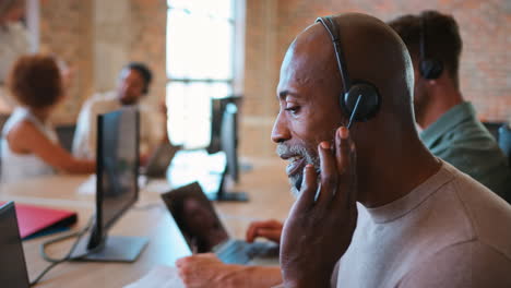 mature businessman in multi-cultural business team wearing headset in customer support centre