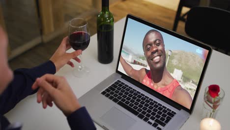 Mid-section-of-african-american-woman-drinking-wine-while-having-a-video-call-on-laptop-at-home