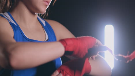 Close-up-of-a-beautiful-athletic-female-boxer-pulls-red-bandages-on-the-hands-of-a-female-fighter.-steadicam-shot