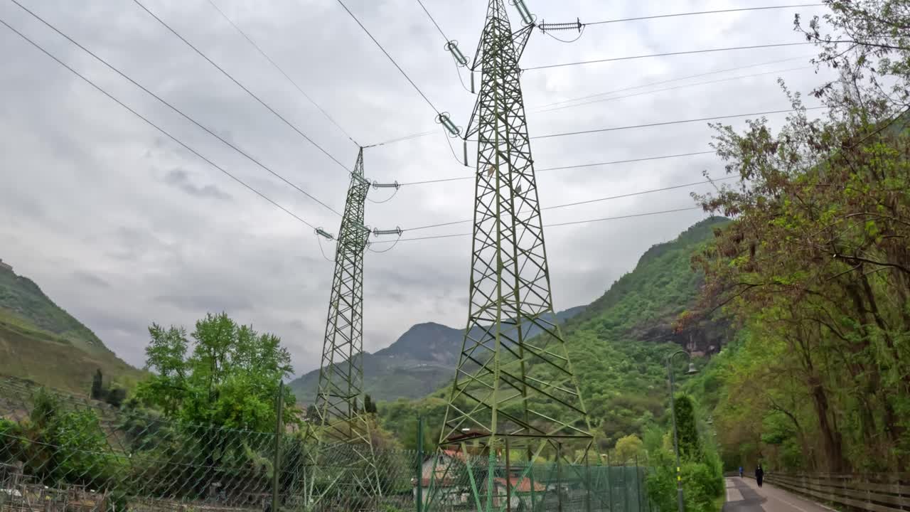 View from below two power towers in lush nature, looking up to a cloudy sky.