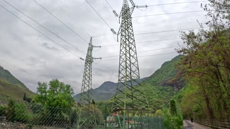 view from below two power towers in lush nature, looking up to a cloudy sky.