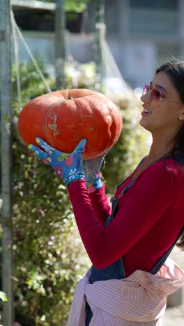 mujer sosteniendo una gran calabaza en un jardín
