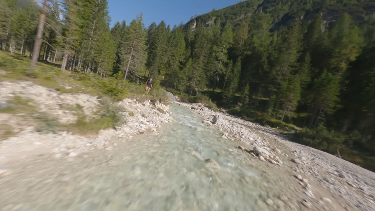 dron fpv volando sobre el arroyo de agua que fluye a través de las montañas en la temporada de verano