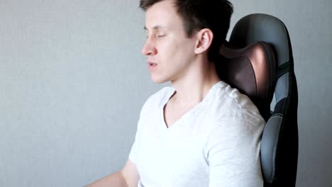un tipo cansado está sentado en el sillón con una almohada de masaje eléctrico.