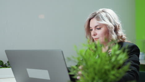 professional woman opens laptop to begin work in bright modern office setting, sitting at desk near architectural model, soft lighting and neutral background