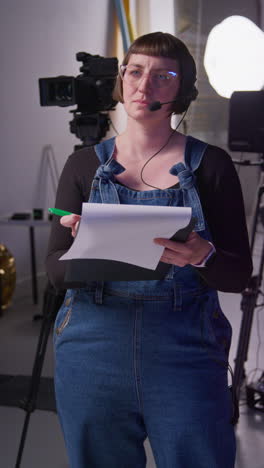 vertical video of female film production assistant with headset and script on movie or video shoot in studio