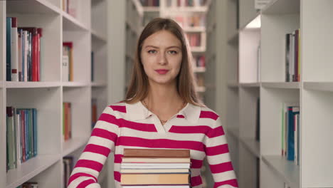 el estudiante sostiene la pila de libros en el pasillo entre las estanterías. la biblioteca bonita muestra literatura para el pedido del cliente en la librería moderna. la dama sonriente con el conjunto de folio