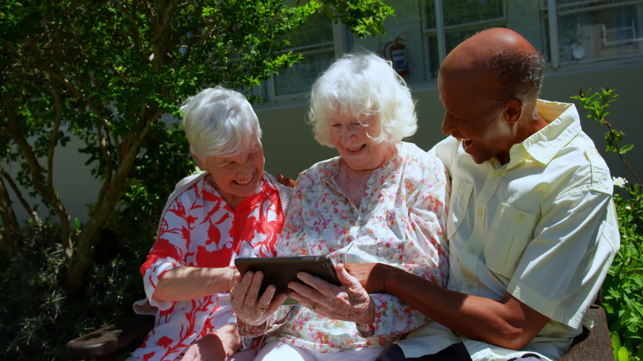 Grupo de amigos idosos ativos de diversas etnias usando tablet digital no jardim de um lar de idosos 4K