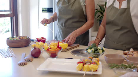 preparing colorful vegetable skewers in kitchen, two diverse senior women enjoying cooking, at home