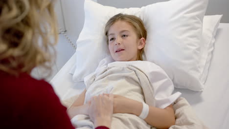 caucasian mother holding hand of smiling daughter patient lying in hospital bed, slow motion