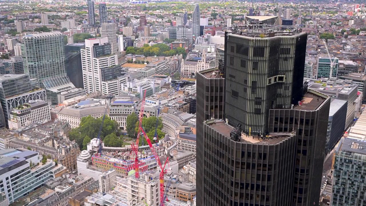 Tower 42 domineert het beeld terwijl de camera uitkijkt over een dichte stadsskyline met kranen en daken eronder