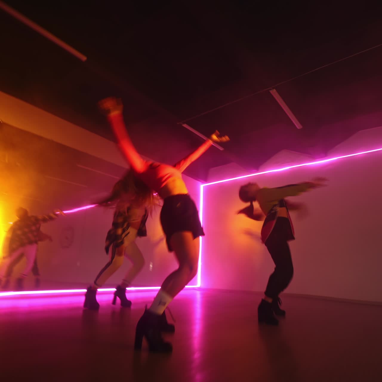Three girls dancing in the studio. Dancers performing indoors in the pink light. Low angle view