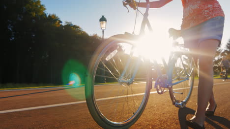 a woman leads a bicycle in the picture one can see the legs and the wheel the sun's rays shine throu