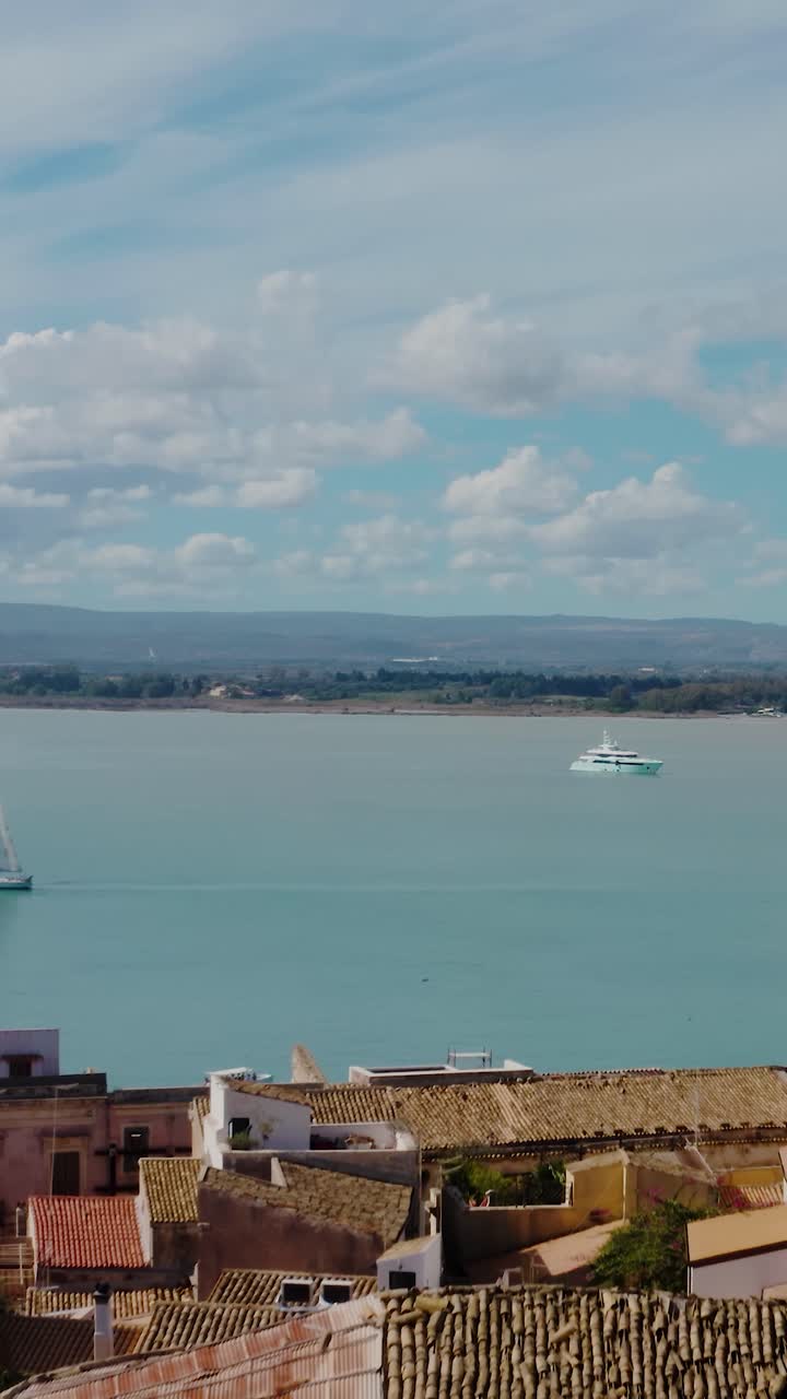 Flying above historic buildings on the island of Ortigia with yacht and boats in the Mediterranean sea. Vertical aerial drone shot of medieval old town in Syracuse, Sicily.