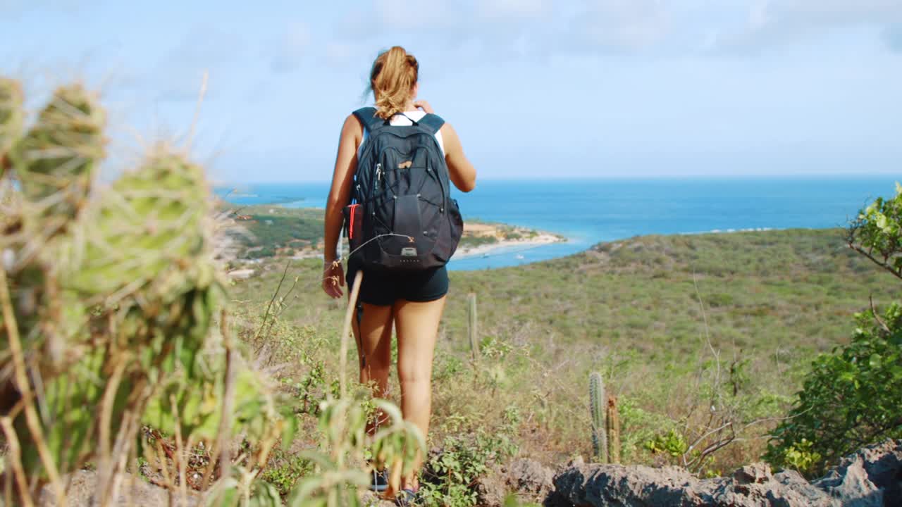 chica con mochila bajando una colina con fondo costero en curacao, caribe