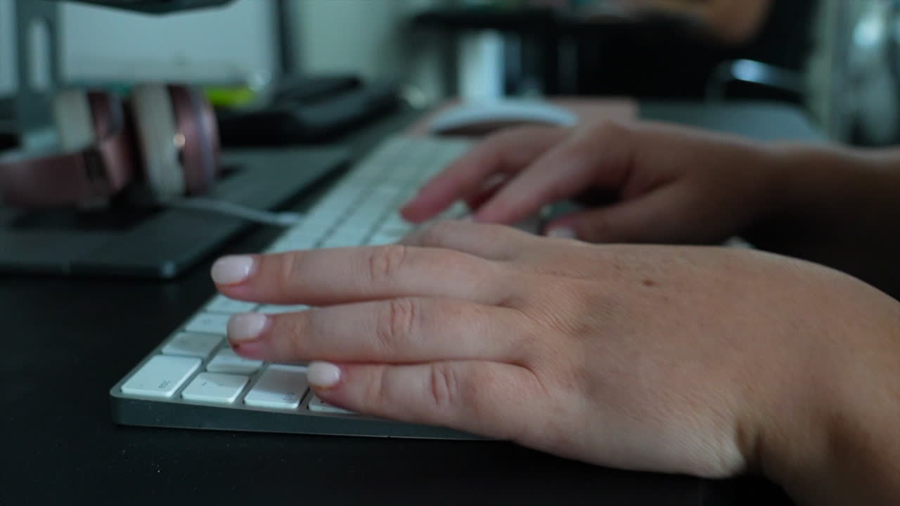 un par de manos femeninas escribiendo en un teclado blanco en una oficina doméstica