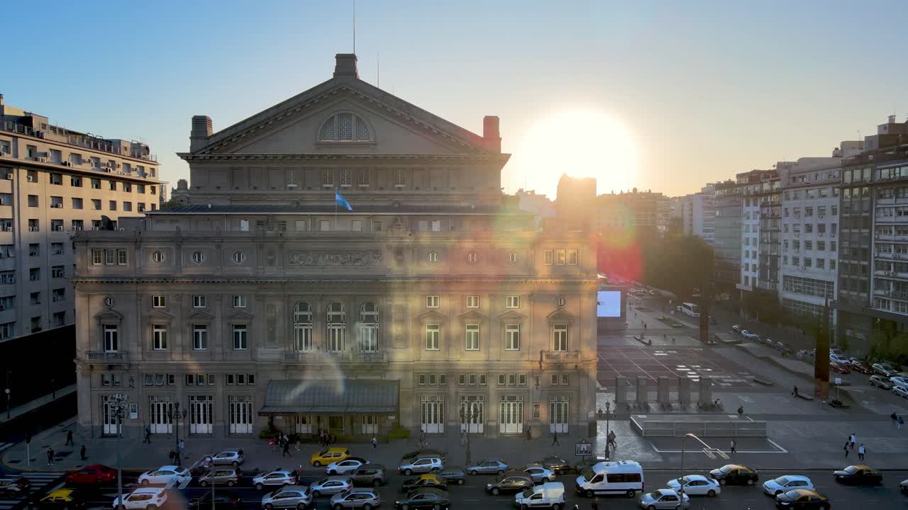 drone de vista aérea volando cerca del edificio de la ópera teatro colón con un gran sol brillante en el fondo al atardecer y tráfico pesado en la avenida 9 de julio en hora punta