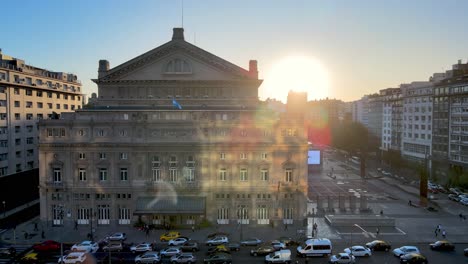 drone de vista aérea volando cerca del edificio de la ópera teatro colón con un gran sol brillante en el fondo al atardecer y tráfico pesado en la avenida 9 de julio en hora punta