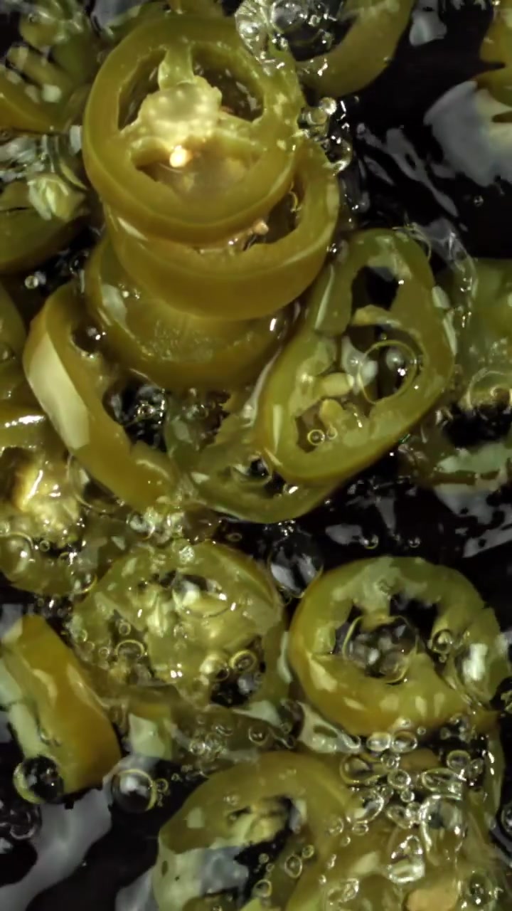 Acqua che schizza al rallentatore su jalapeños verdi freschi affettati