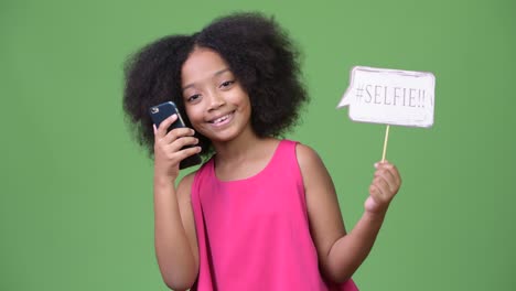 young cute african girl with afro hair taking selfie with paper sign