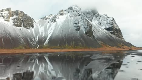 using a 4k drone, capturing cinematic, distinctive, and striking footage of a towering rocky mountain casting an enchanting reflection onto the melting ice water below