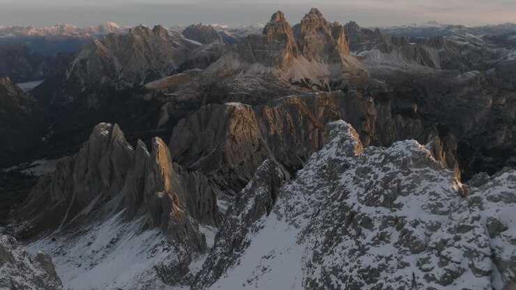 Spettacolari riprese con drone che scendono sopra le imponenti cime calcaree delle Dolomiti coperte di neve invernale. La luce dell'ora d'oro illumina le maestose pareti rocciose e le scogliere frastagliate