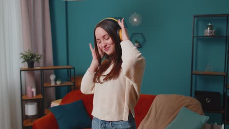 overjoyed young woman in wireless headphones dancing singing on cozy couch in living room at home