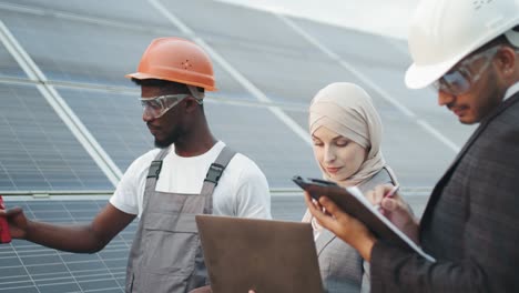 industrial worker showing thermal imager with indexes to inspectors. inspection on solar station. muslim woman and indian man standing with african technician and checking temperature of solar panels