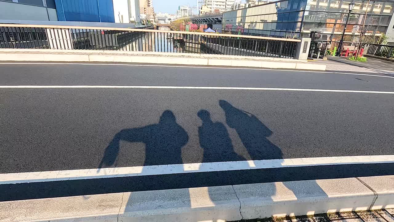 Shadows of two people on a bridge in Tokyo with a cyclist passing by. Bright daylight enhances the urban scene