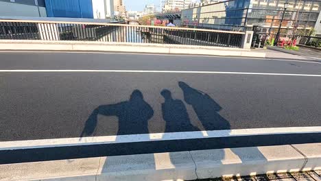 shadows of two people on a bridge in tokyo with a cyclist passing by. bright daylight enhances the urban scene